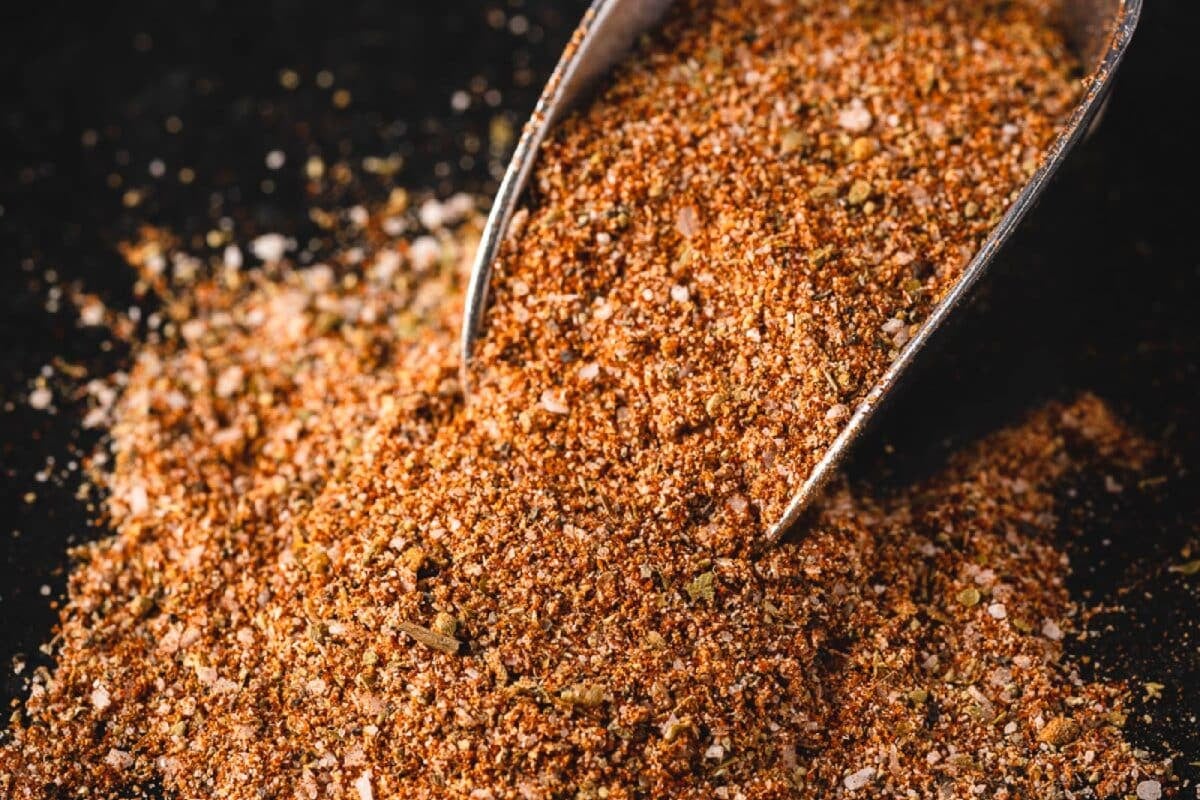 A pile of cajun seasoning for seafood recipes with a metal scoop in it.