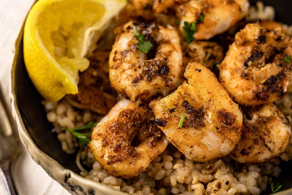 Cajun grilled shrimp on a black plate with a lemon wedge.