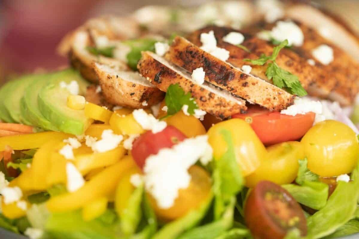 Sliced chicken breast pieces on a bed of lettuce and other sliced veggies.