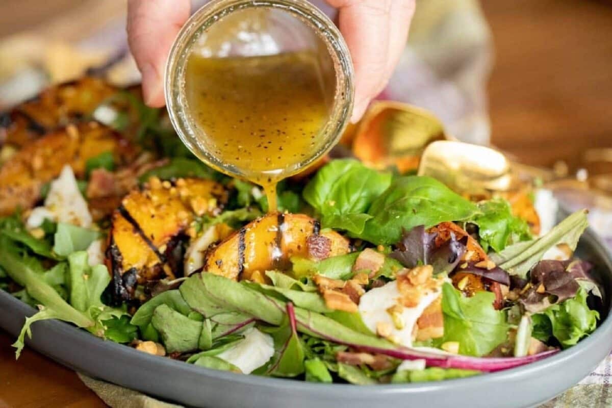 A green salad with grilled peaches being drizzled with dressing from a jar.