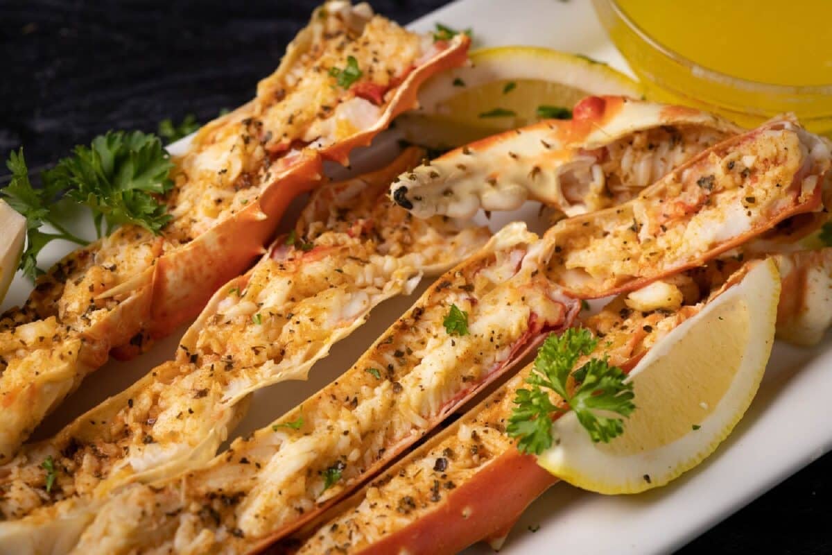 Grilled grab legs sprinkled with seafood seasoning on a platter with a lemon wedge.