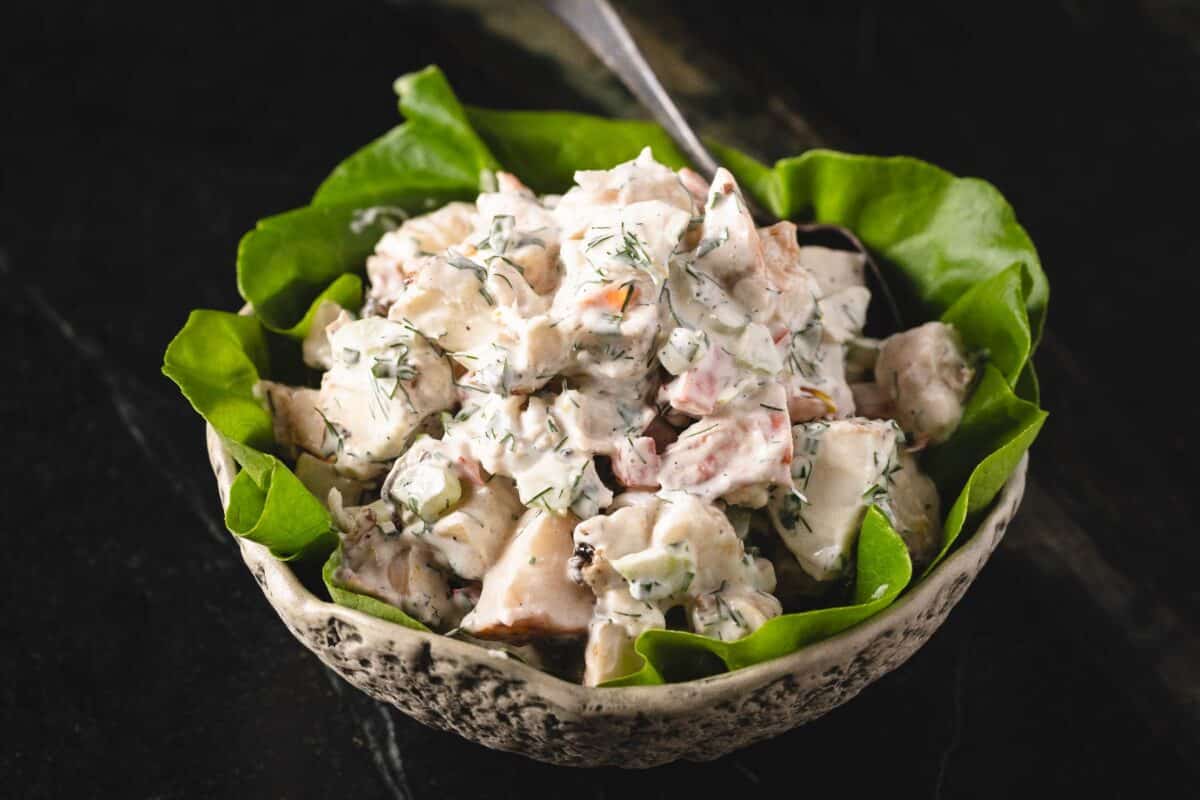 Lobster salad on a bed of lettuce in a white speckled bowl.