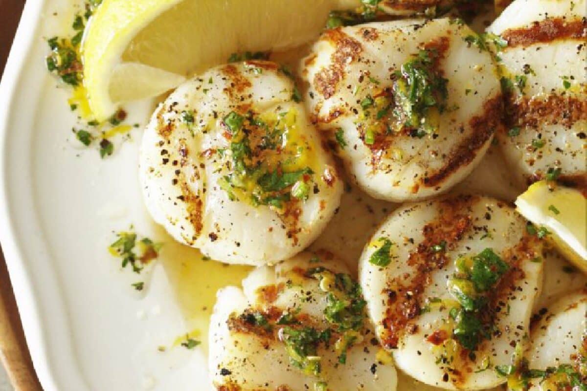 Grilled scallops on a plate with lemon wedges, sprinkled with seafood seasoning.