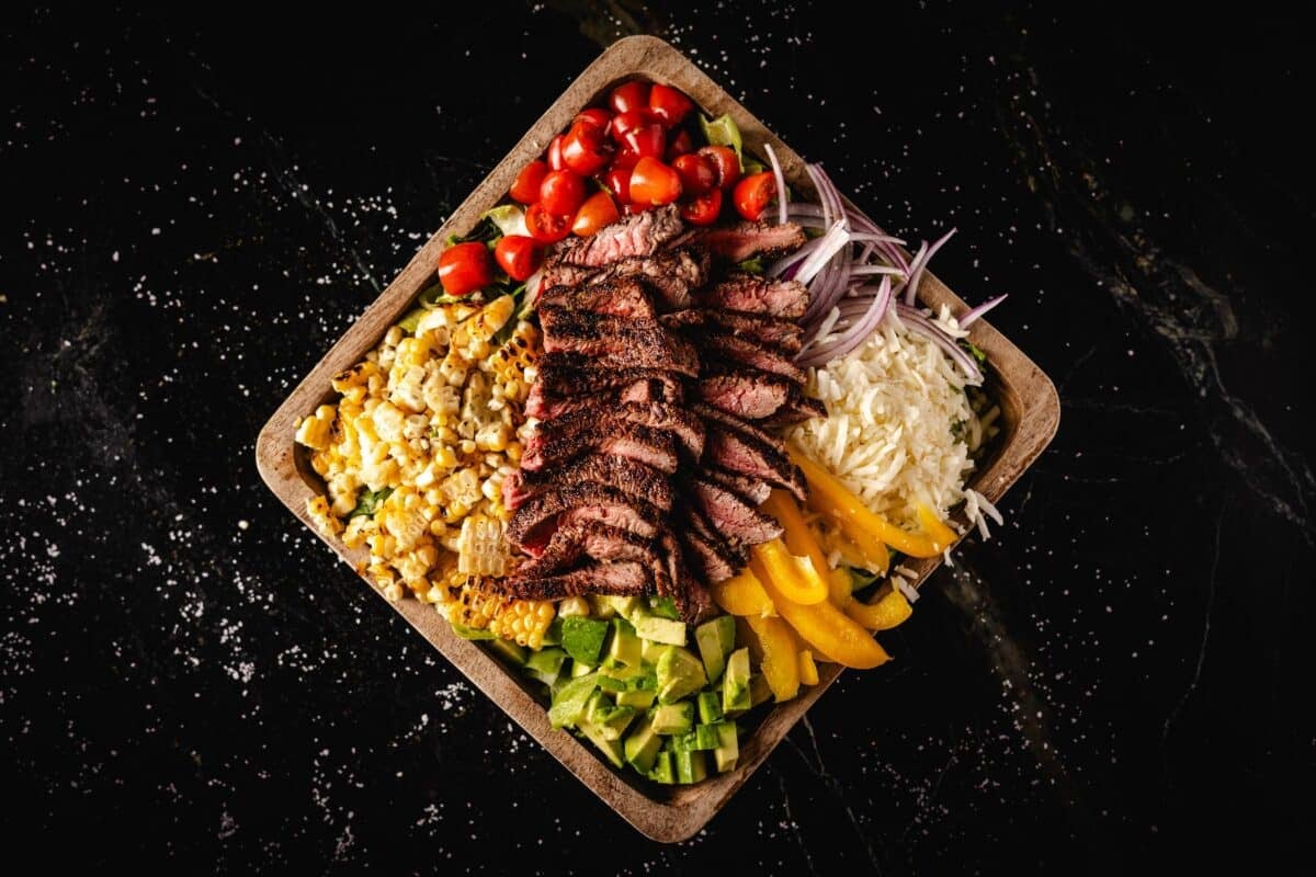 A wooden platter topped with sliced steak and veggies.