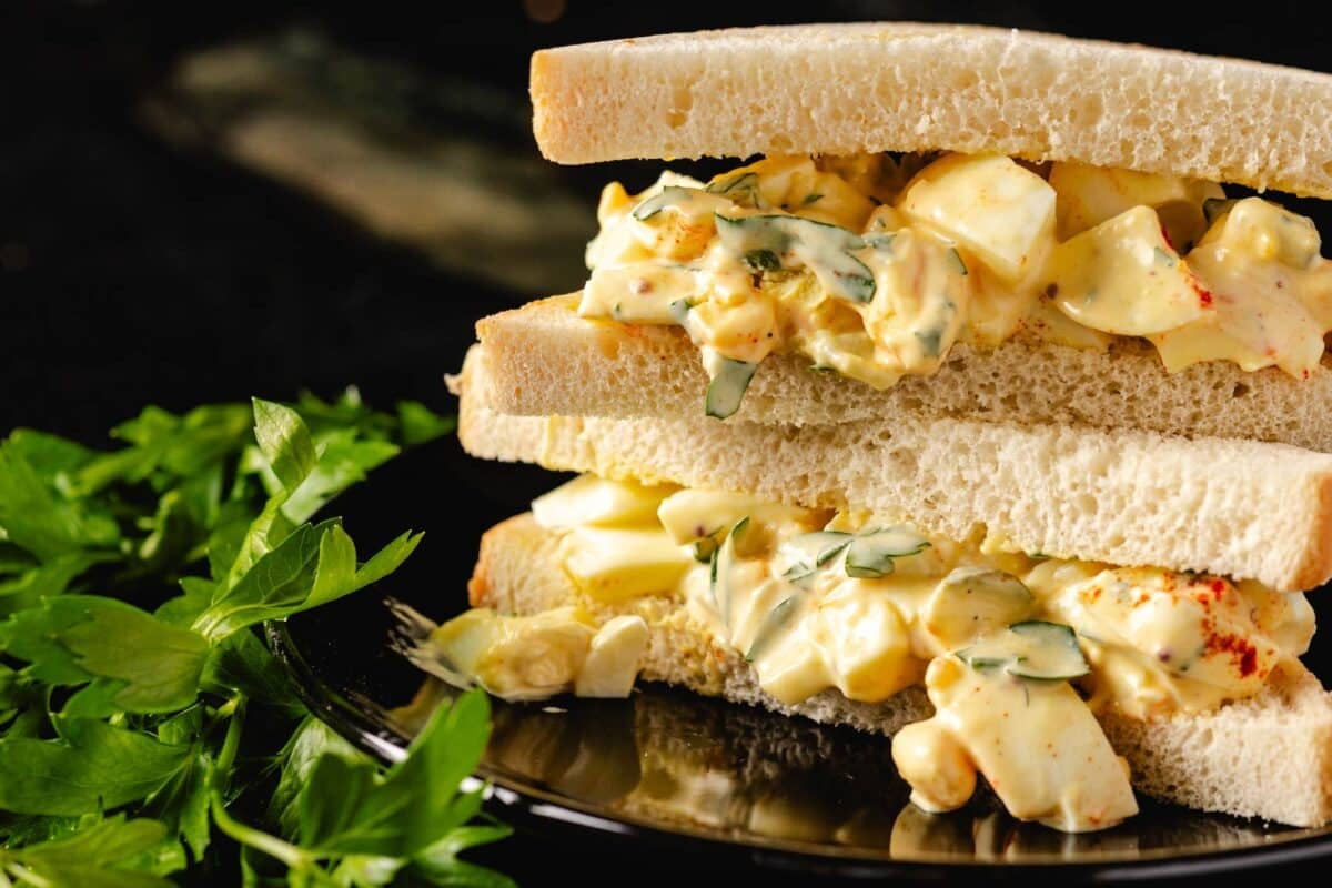 An egg salad sandwich on a reflective platter.