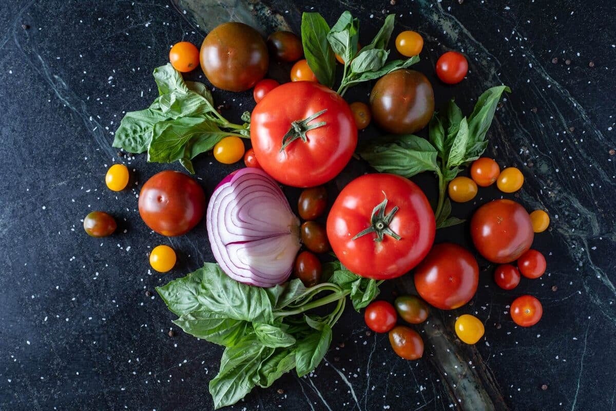 Fresh tomatoes, onions, and leafy greens on a black counter.