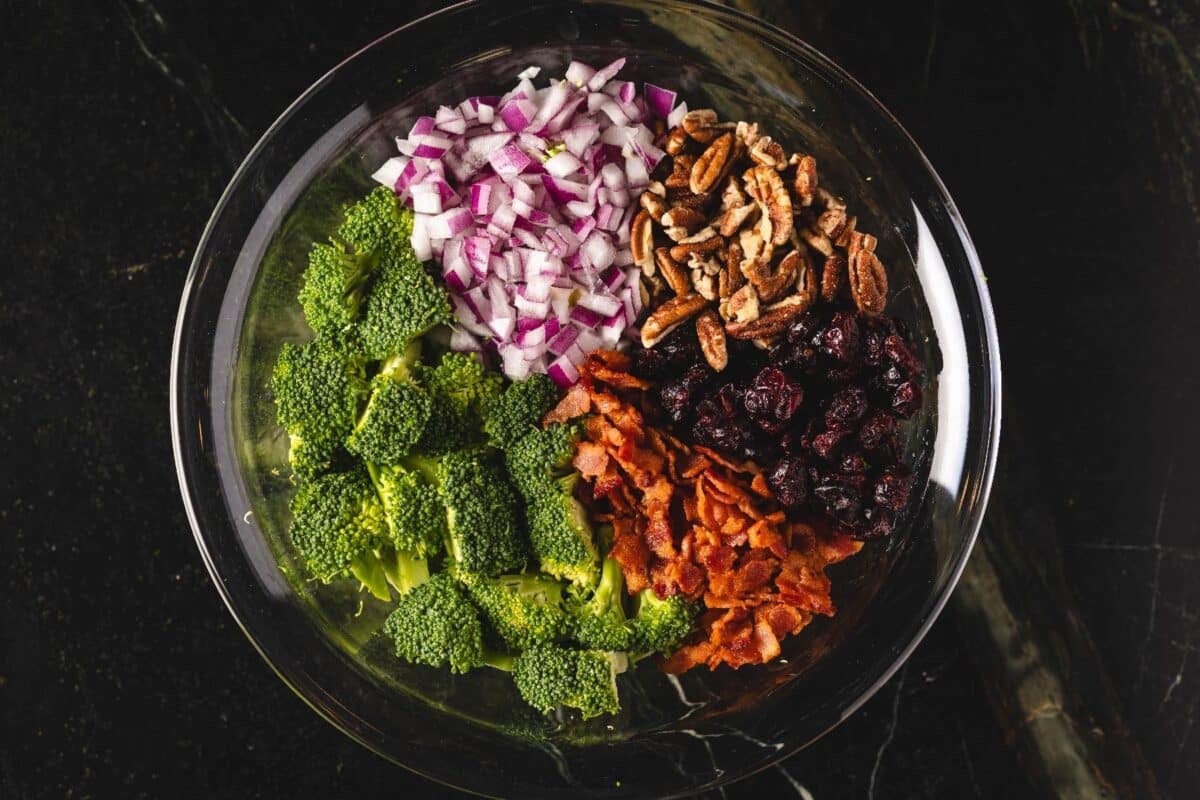 Chopped broccoli, onions, and nuts in a glass bowl.