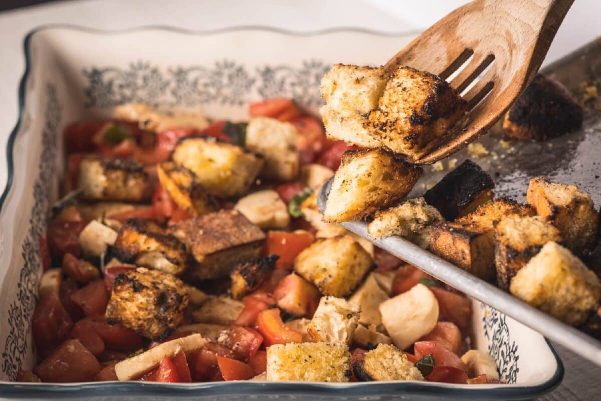 A platter full of panzanella salad being stirred with a wooden spoon.