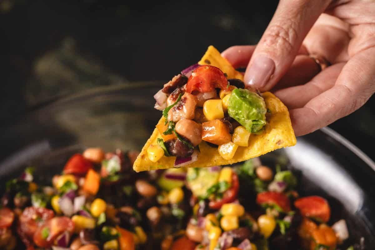 A chip holding salsa above a bowl of more salsa.