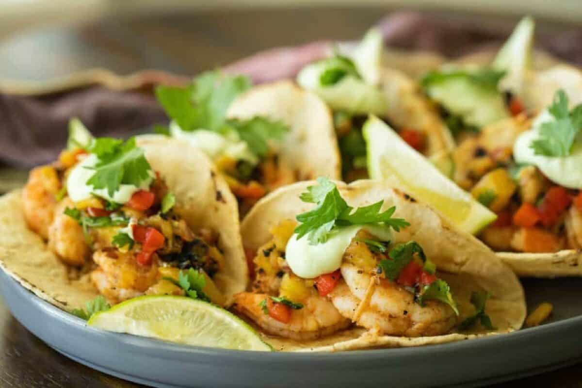 Shrimp tacos on a plate with scoops of pineapple salsa.