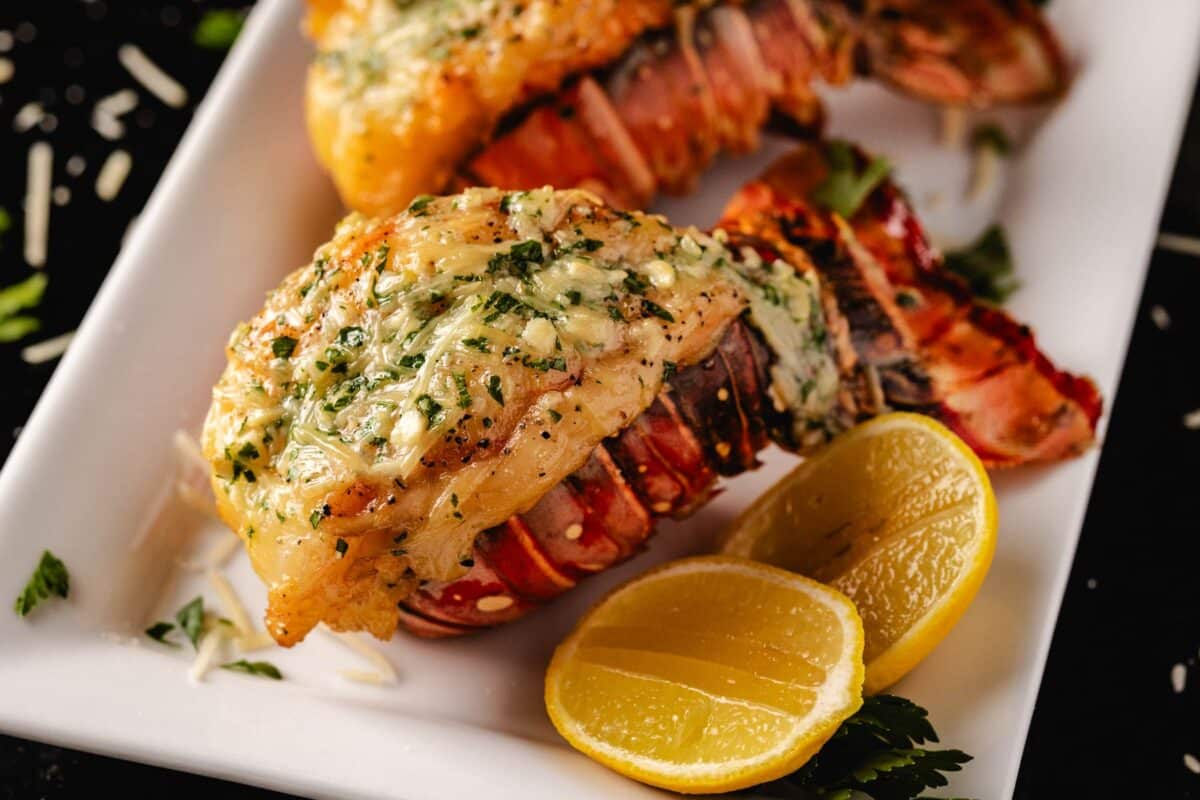 Smoked lobster tails on a white plate garnished with lemon halves.