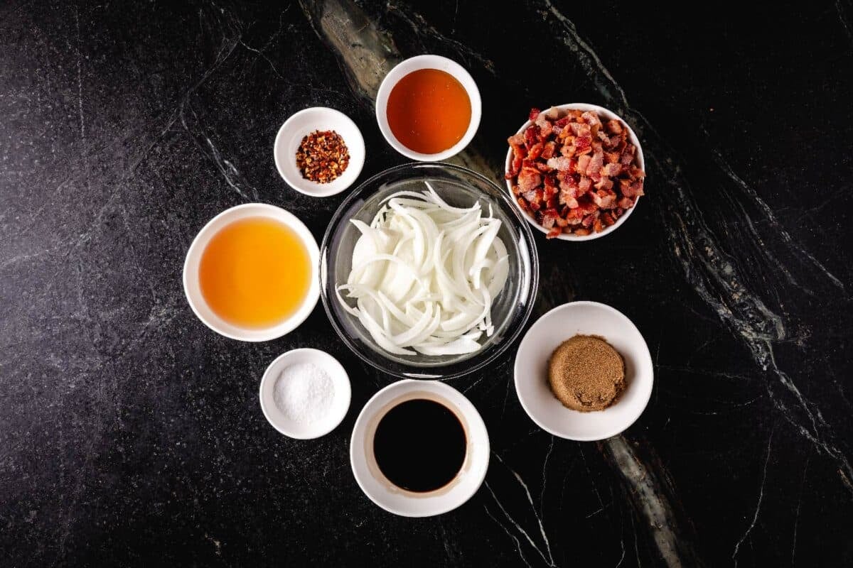 Sliced onions and other raw ingredients in glass bowls on a marble countertop.