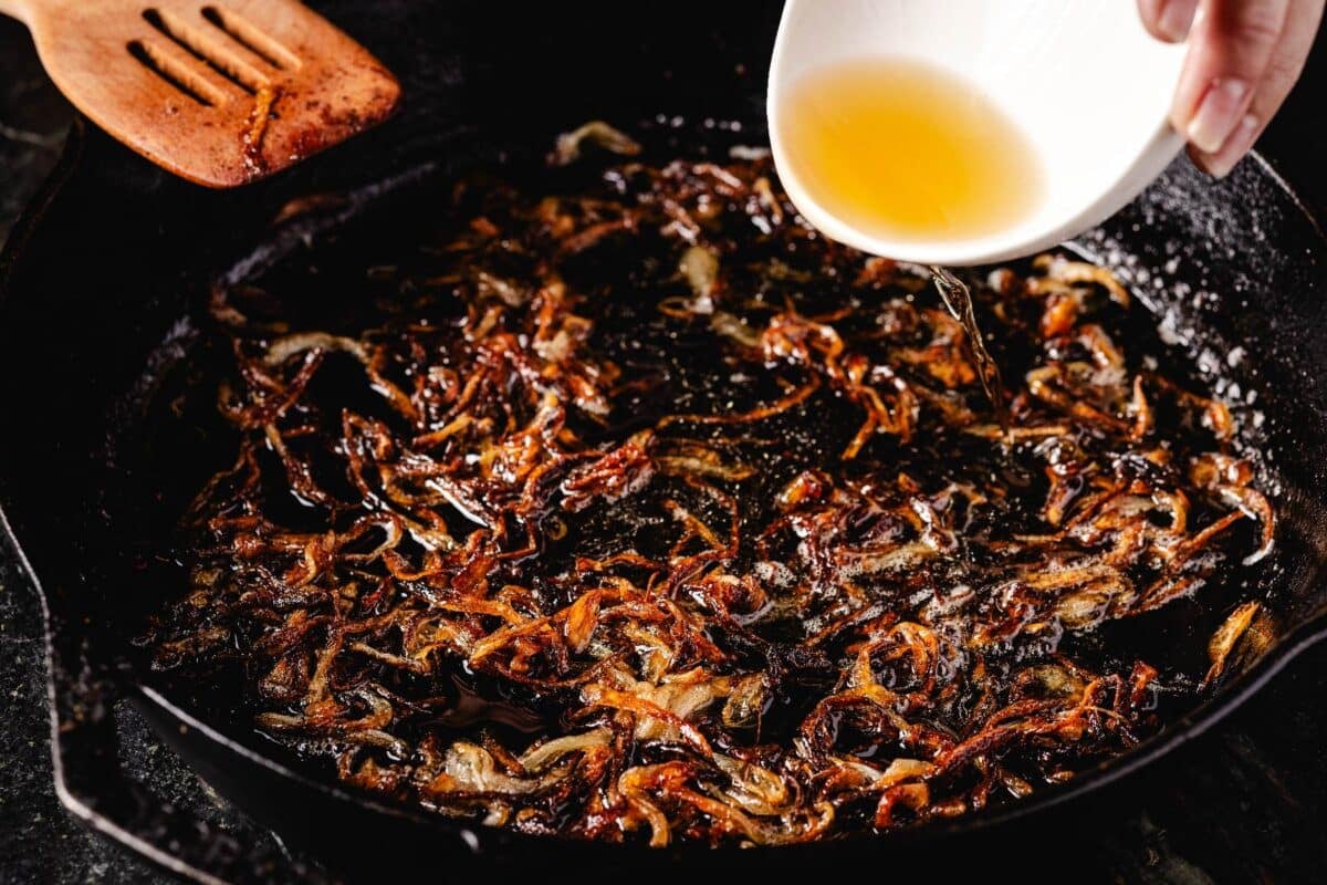 Whiskey in a bowl being poured onto pork in a cast iron skillet.