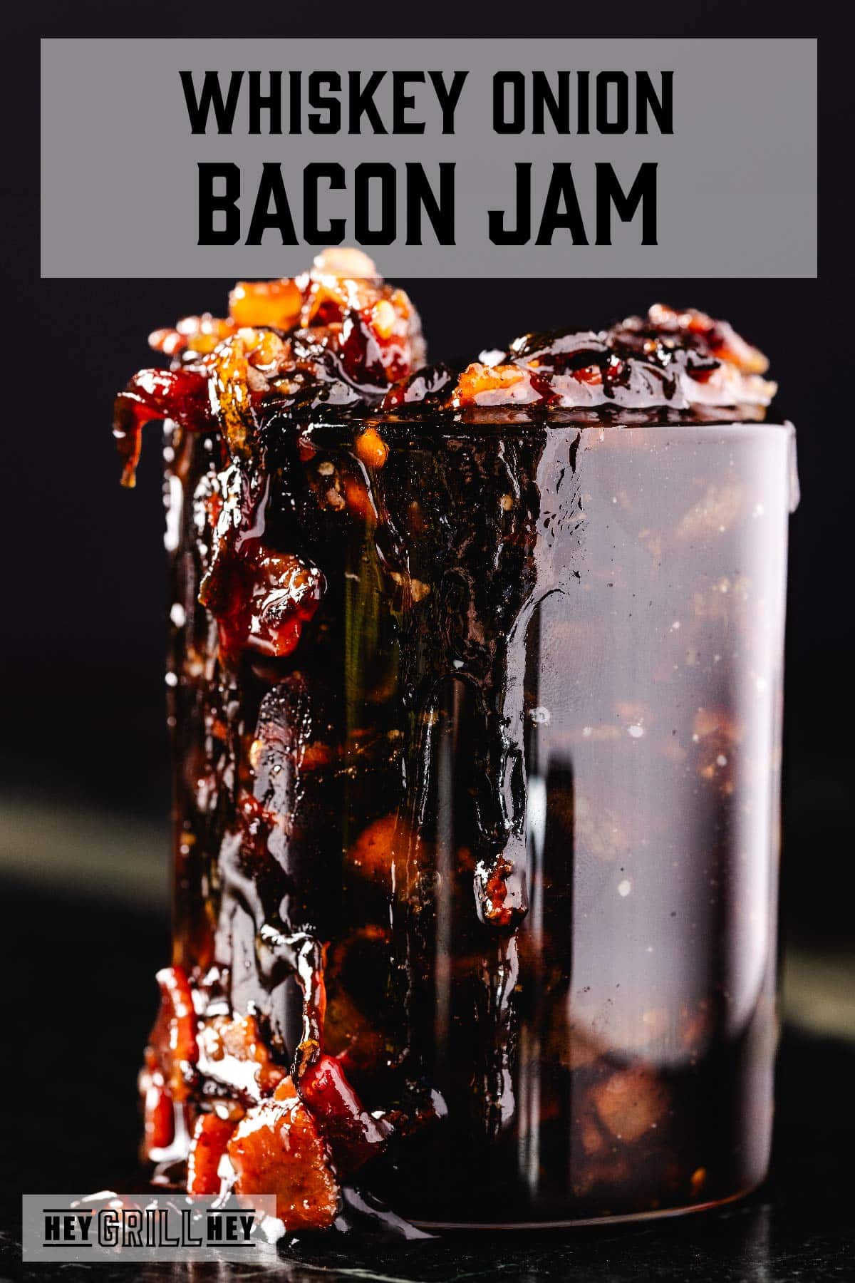 A mason jar overflowing with bacon jam. The text overlay reads "Whiskey Onion Bacon Jam" at the top, and "Hey Grill Hey" at the bottom.