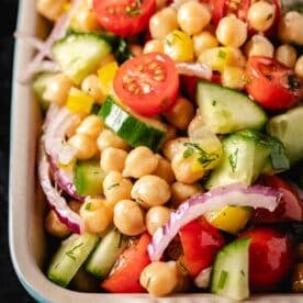 A salad of cherry tomatoes, sliced cucumbers and red onions, and garbanzo beans on a plate.