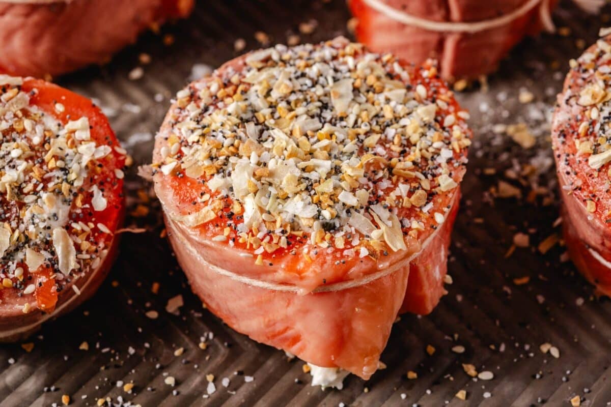 Salmon fillets rolled and tied with butcher's twine and sprinkled with seasoning, sitting on a baking sheet.