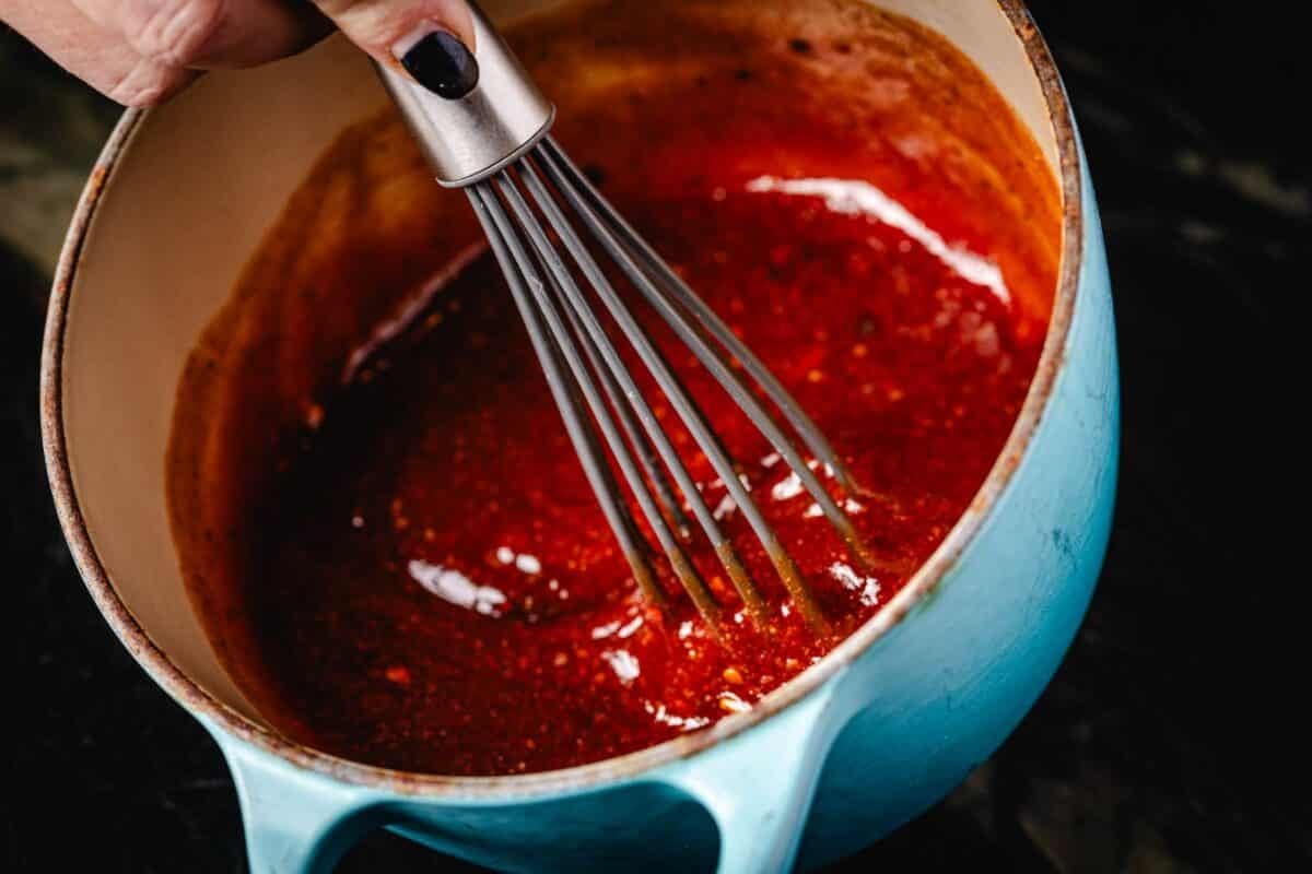 A whisk mixing BBQ sauce in a blue pot.