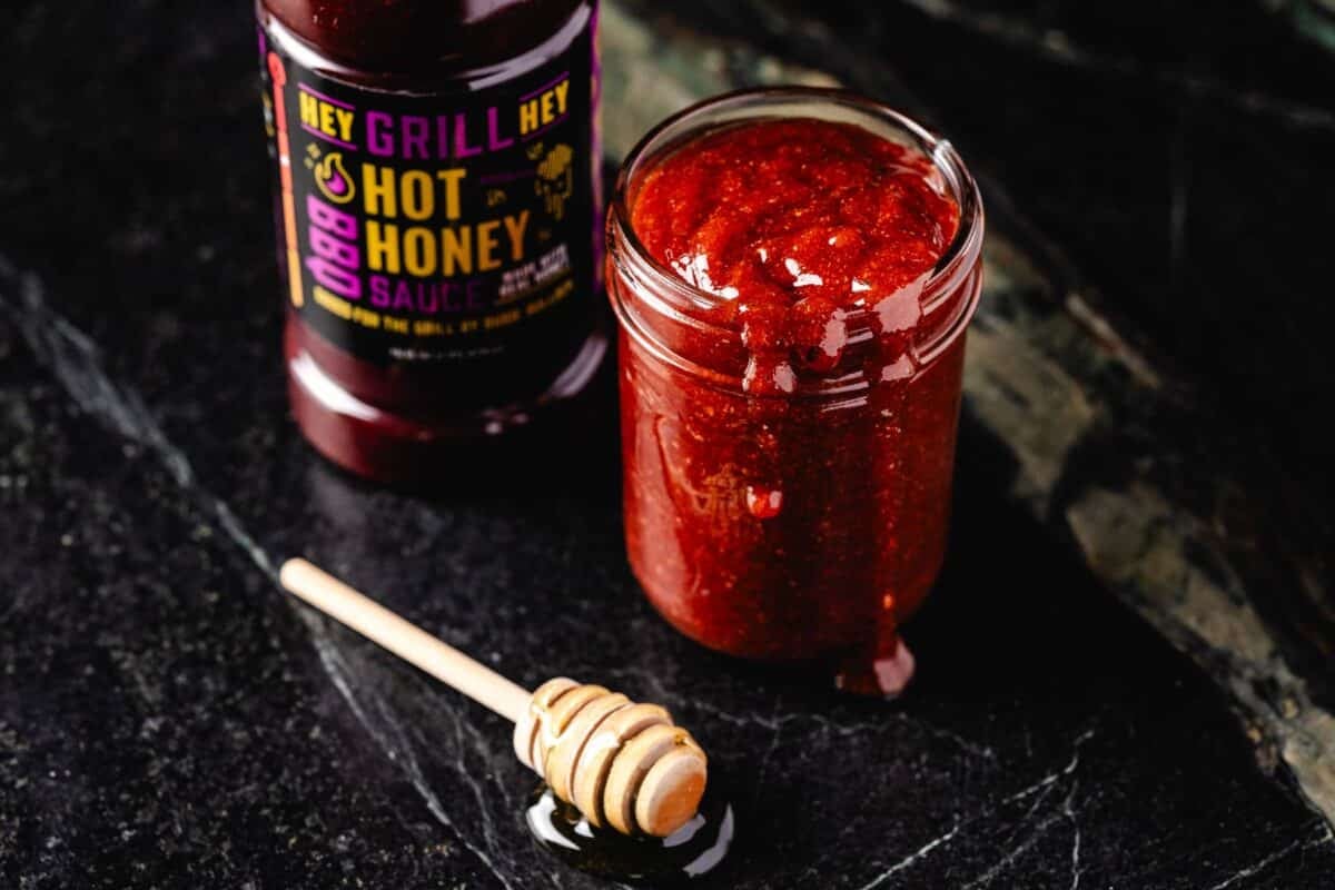 A bottle and jar of BBQ sauce on a counter next to a honey dipper.