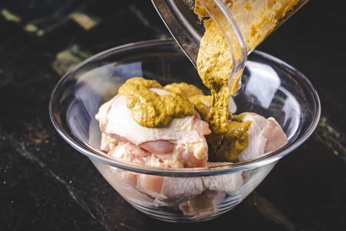 Chicken in a glass bowl, with a cup of sauce being poured onto it.