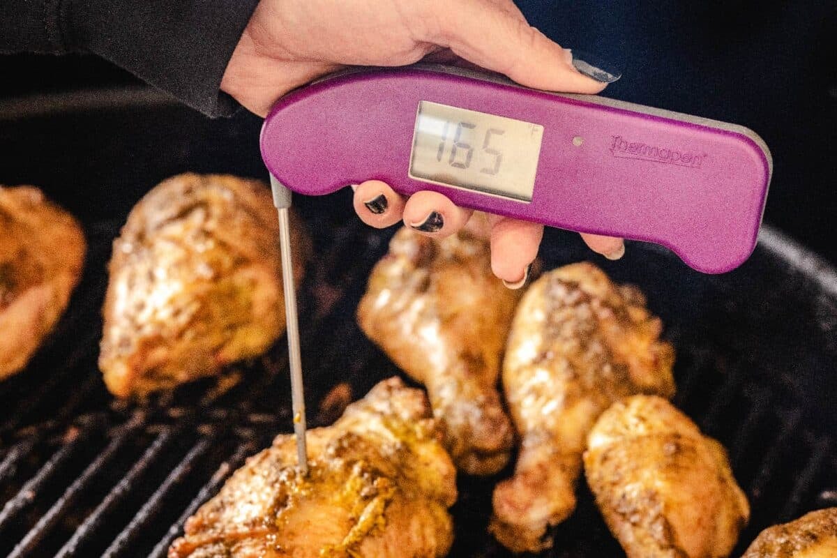 Jerk chicken legs and thighs on the grill with a thermometer reading 165 degrees F probing one piece.