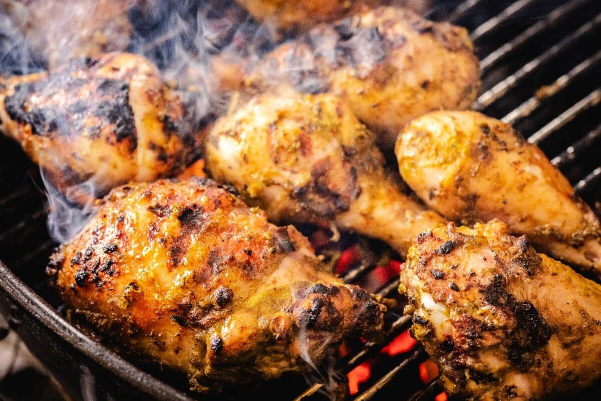 Chicken legs and thighs on grill grates over hot charcoal.