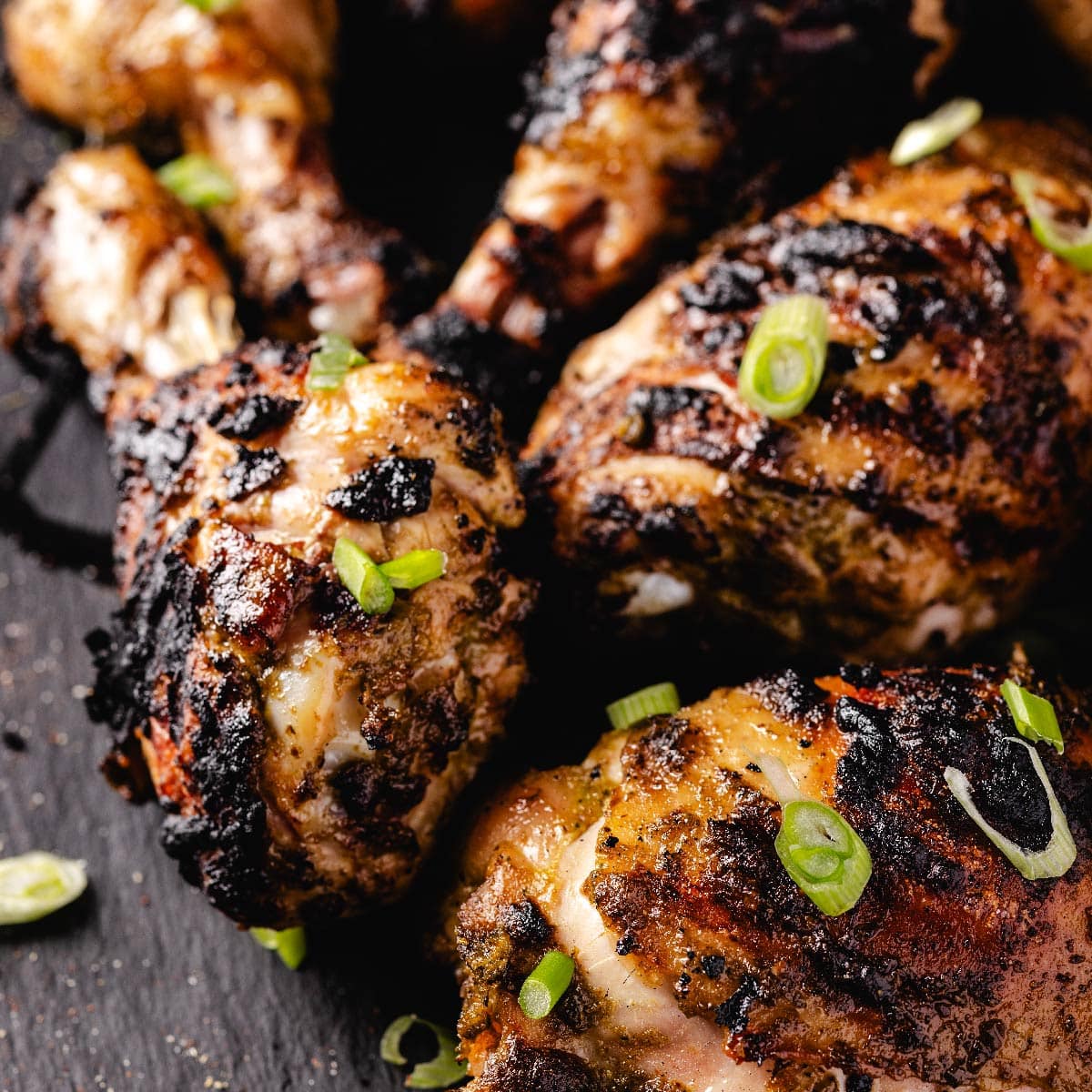 Char-grilled chicken drumsticks and thighs garnished with sliced green onions.