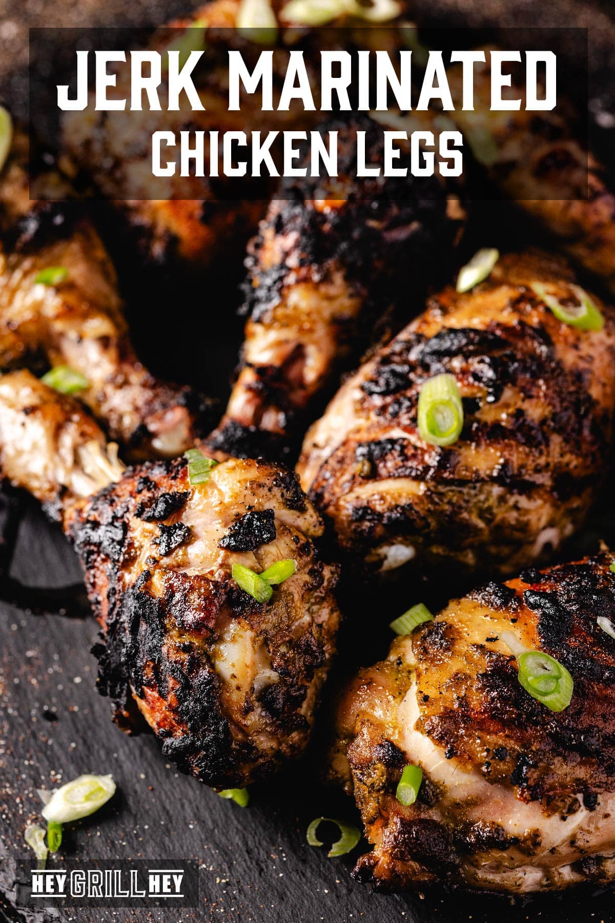 Char-grilled chicken legs and thighs on a black surface. The text overlay reads "Jerk Marinated Chicken Legs" at the top, and "Hey Grill Hey" at the bottom.