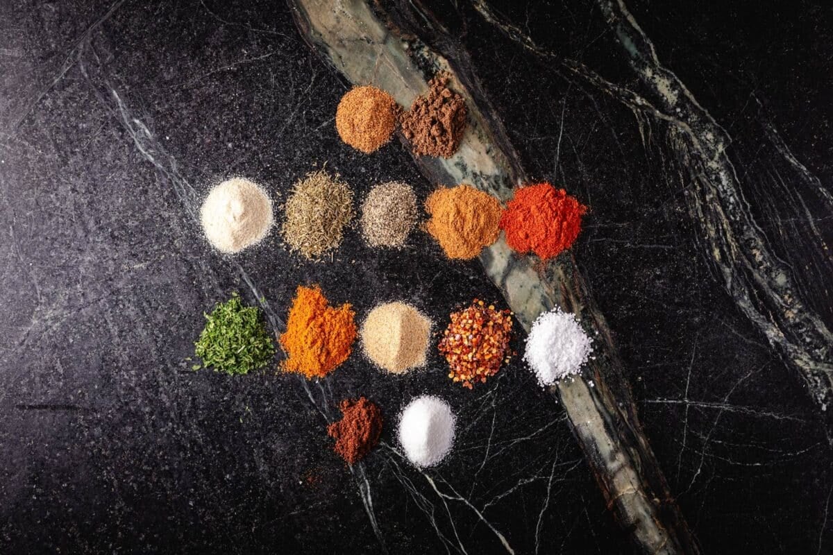 14 separate, small piles of various seasonings on a marbled countertop.