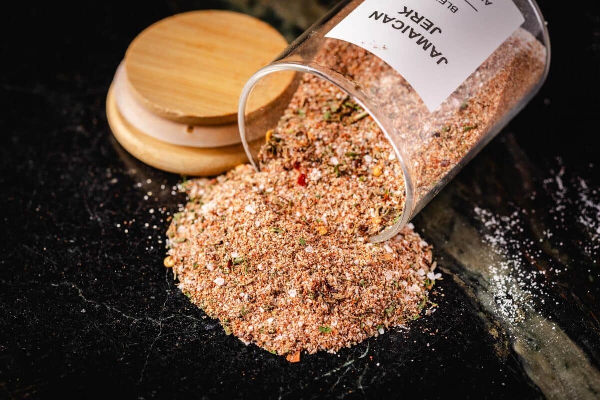 A jar of seasoning tipped over next to the lid, spilling onto a countertop.