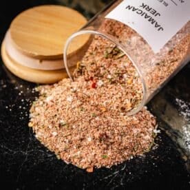 A jar of seasoning tipped over next to the lid, spilling onto a countertop.