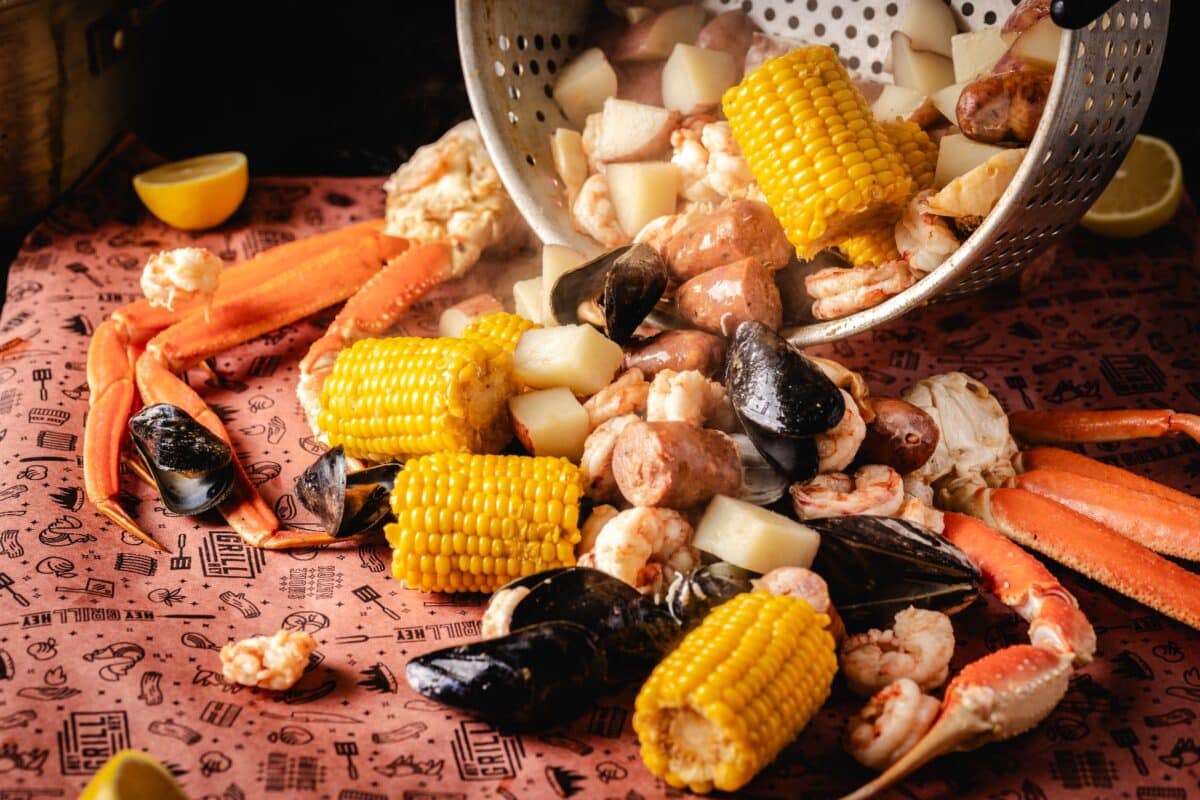 A seafood boil of crab, corn, sausage and more, being poured from a pot onto butcher paper.