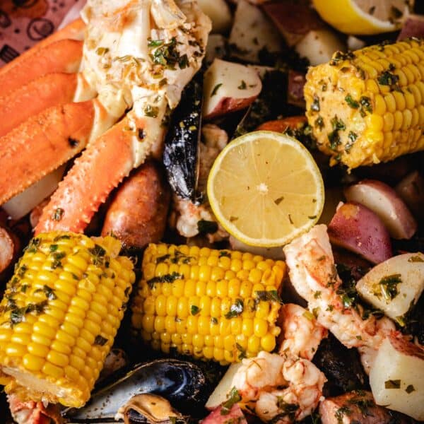 A crab boil including crab legs, corn cobs, lemon, and potatoes, poured onto butcher paper.