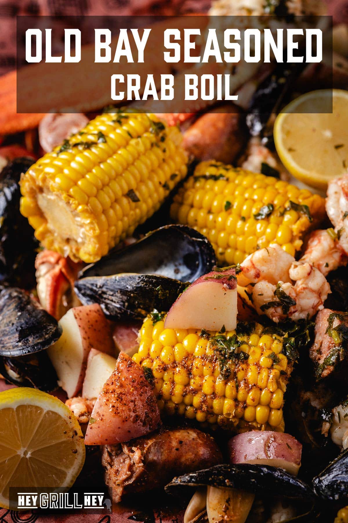 A seafood and veggie boil piled on newspaper. The text overlay reads "Old Bay Seasoned Crab Boil" at the top, and "Hey Grill Hey" at the bottom.