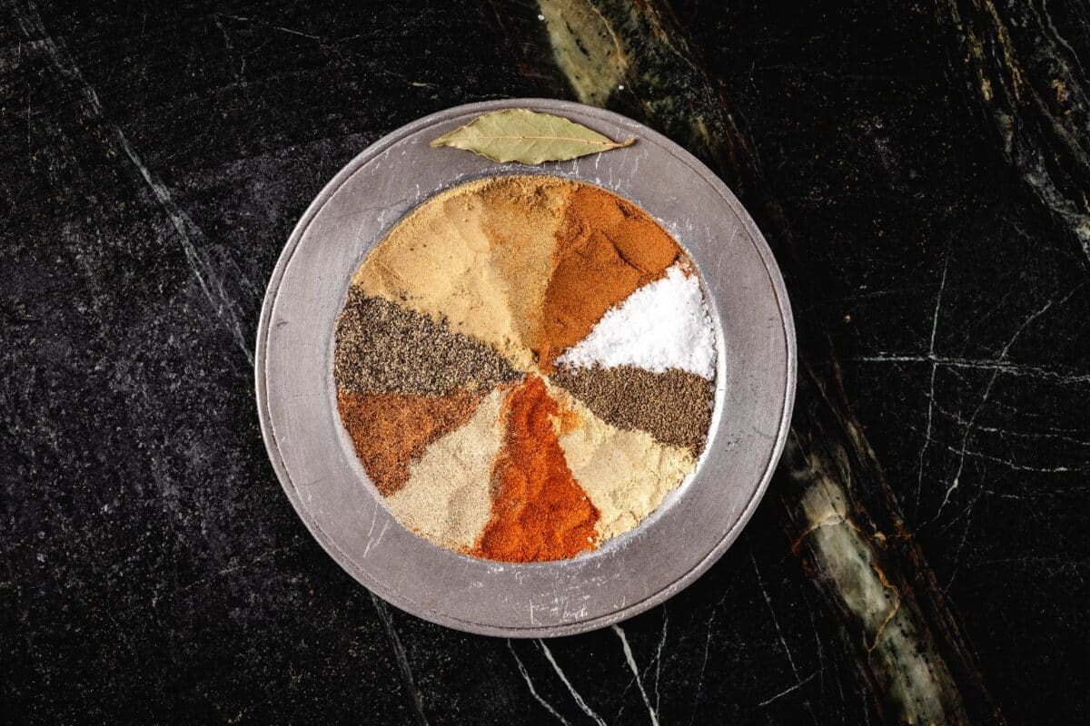 An overhead shot of a metal plate with seasonings in a pattern, and a bay leaf on the rim.