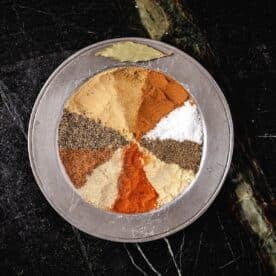 An overhead shot of a metal plate with seasonings in a pattern, and a bay leaf on the rim.