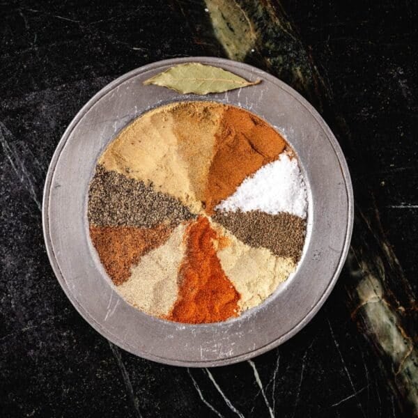 An overhead shot of a metal plate with seasonings in a pattern, and a bay leaf on the rim.