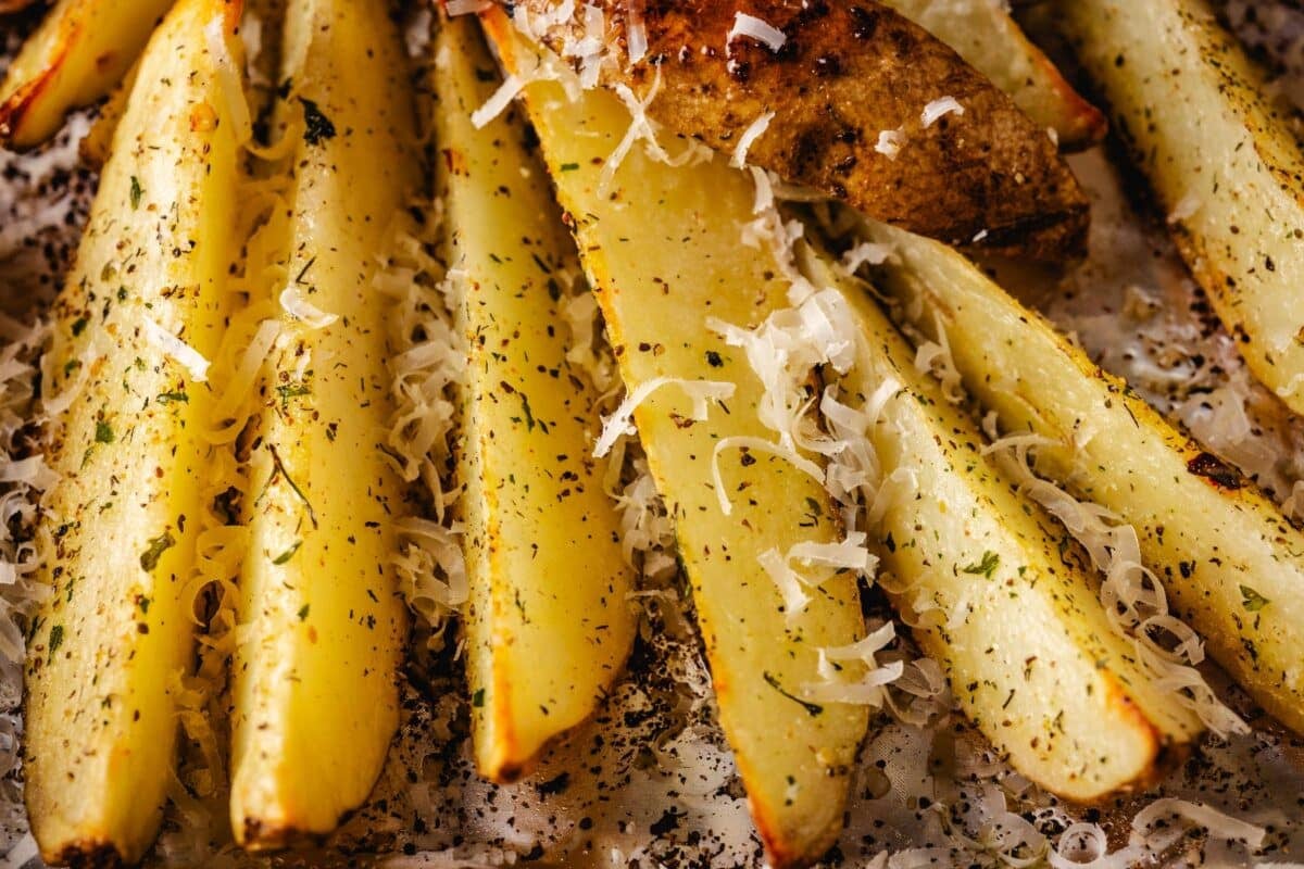 Thick-cut fries on a baking sheet sprinkled with seasoning and parmesan cheese.