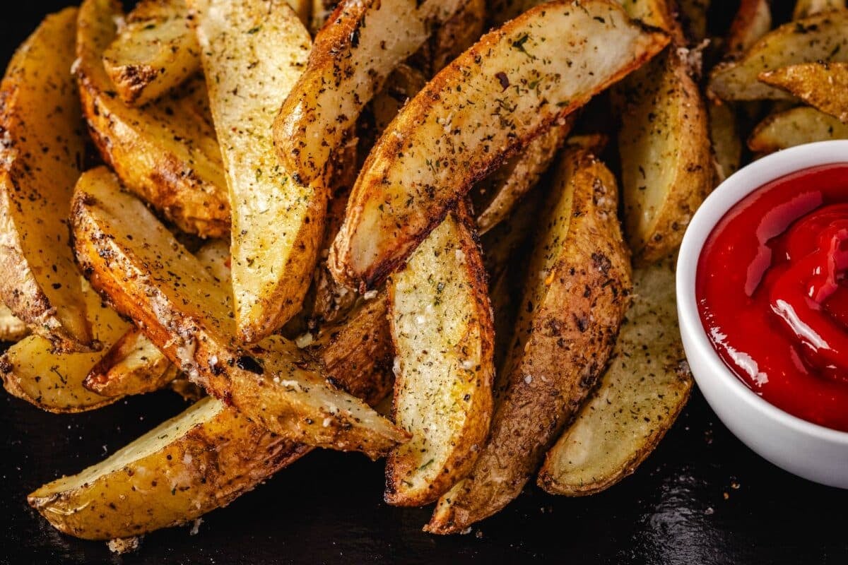 Roasted potato wedges stacked next to a cup of ketchup.