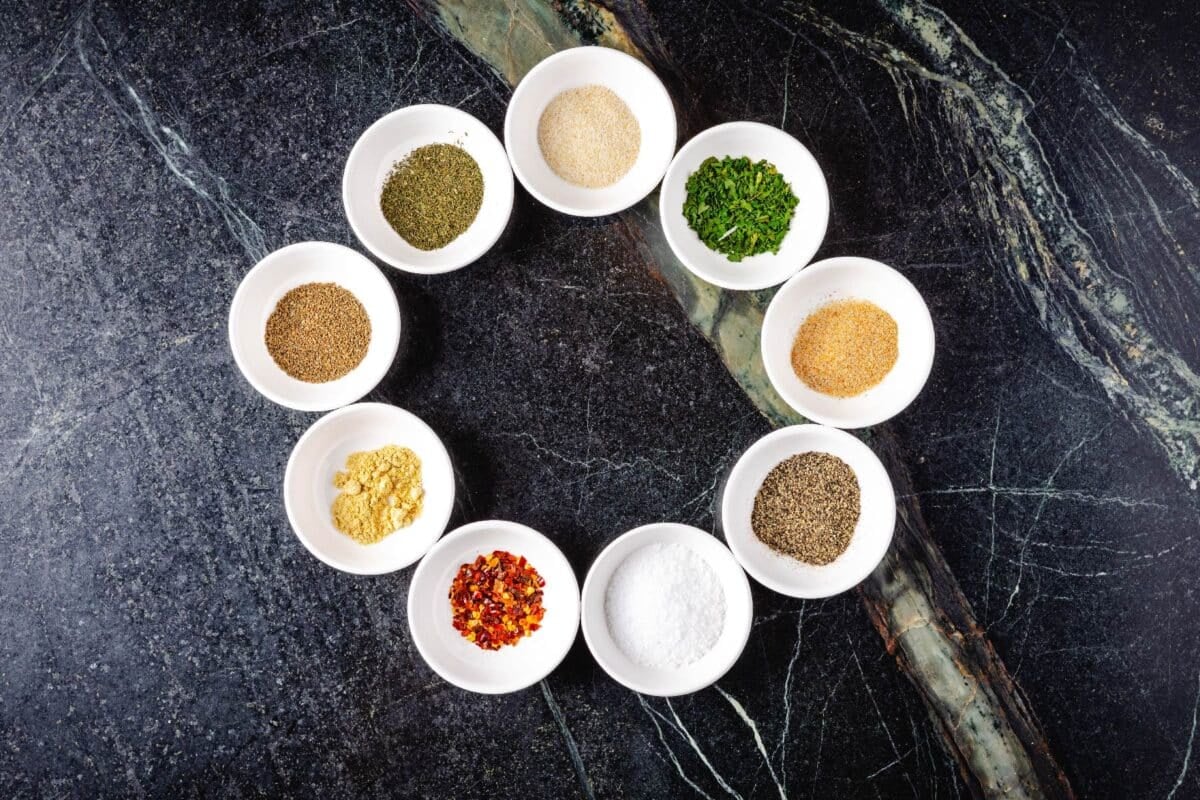 White glass bowls in a circle filled with spices and herbs.