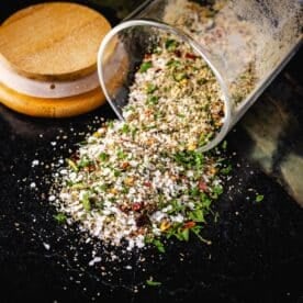 A glass jar tipped on its side with a spice blend pouring out onto a table.