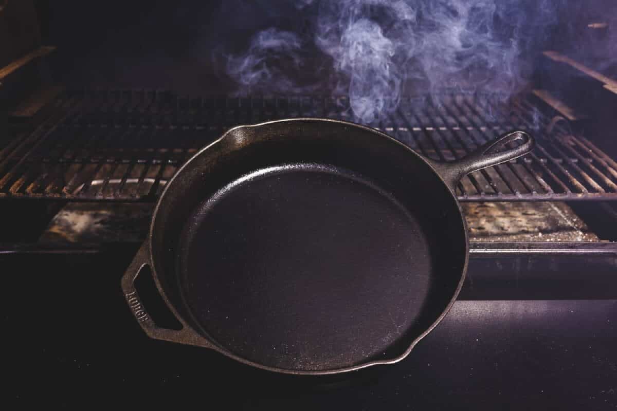 A skillet sitting in front of smoker grates with smoke rising behind it.