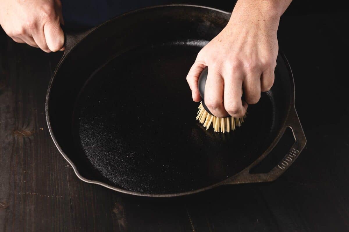 A hand using a brush to clean out the inside of a pan.