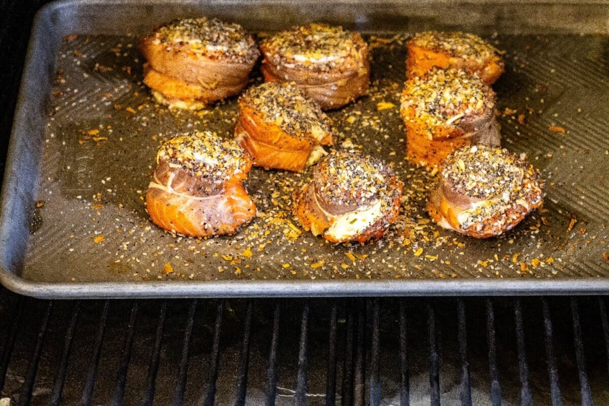 A baking sheet lined with salmon pinwheels on the grates of a smoker.