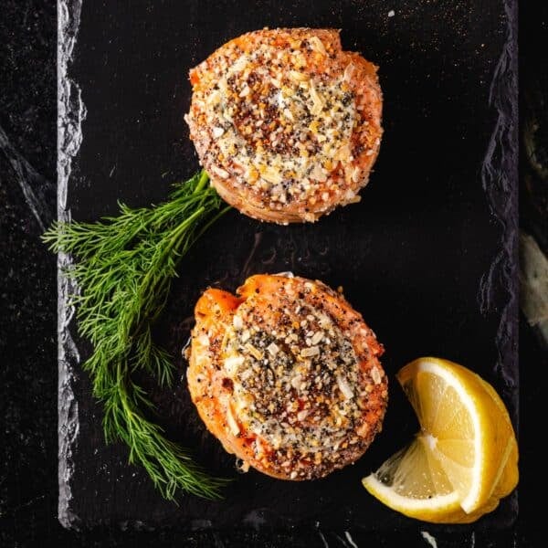 Smoked salmon pinwheels on a black platter with fresh dill and lemon wedges.