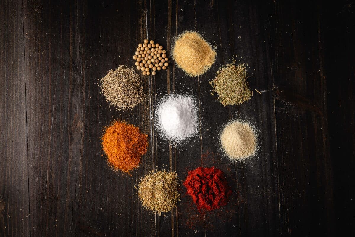 A small pile of salt on a tabletop, surrounded by a circle of 8 more piles of various spices.