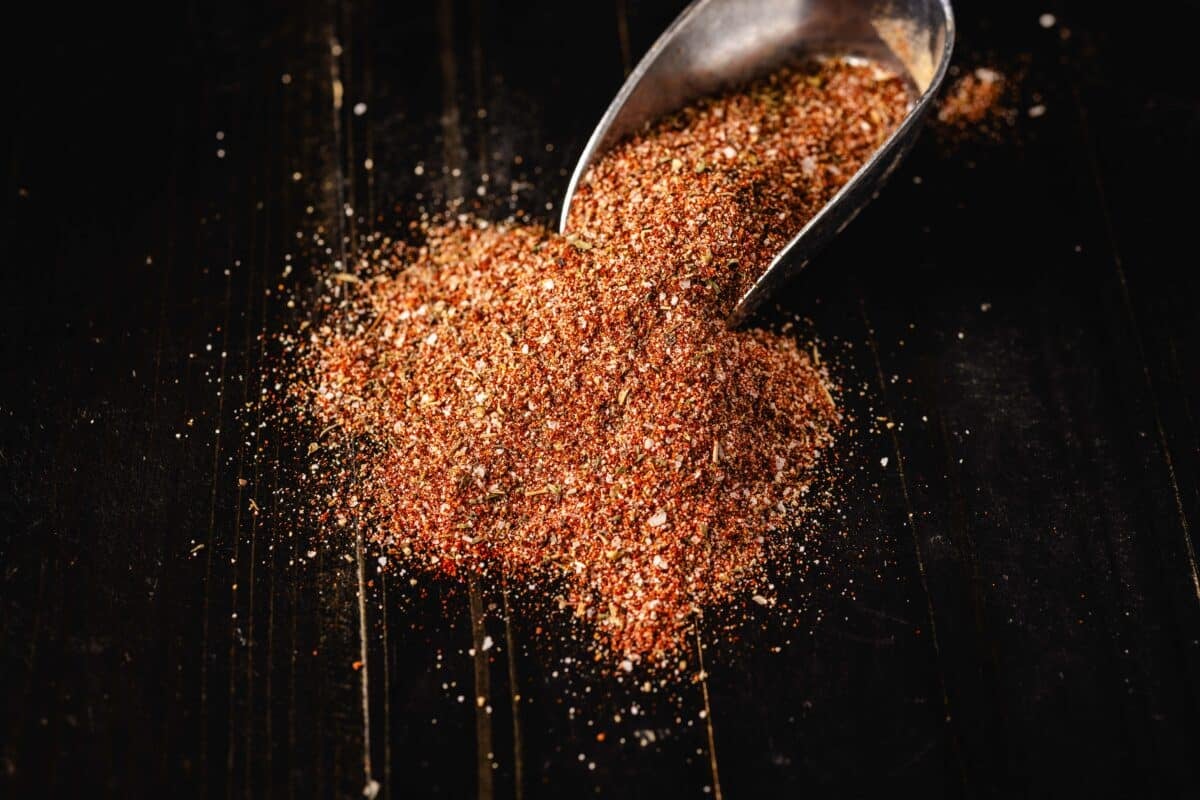 A metal scoop full of seasoning spilling out onto a table.