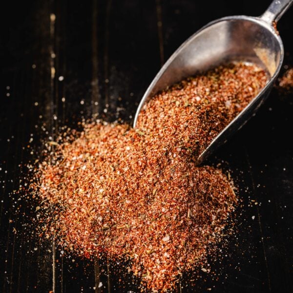 A metal scoop resting in a pile of blackened seasoning on a black countertop.