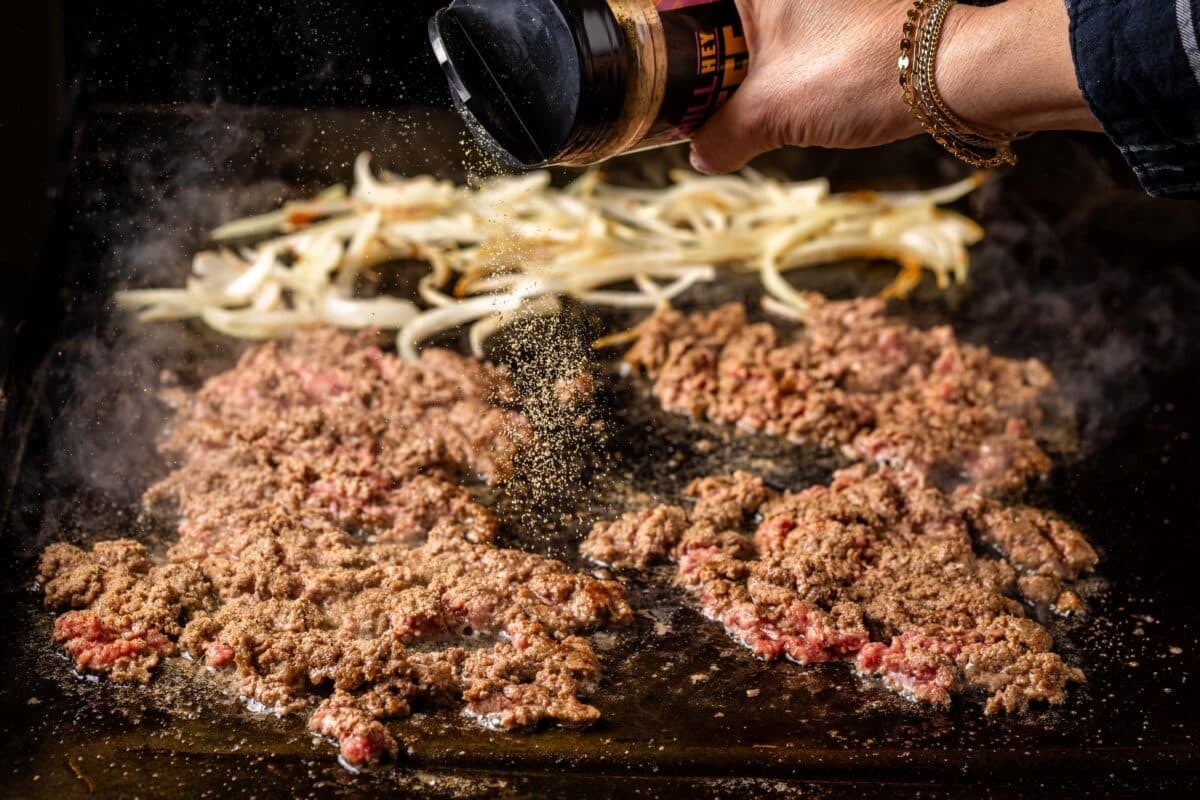 A flat-top grill with ground been and sliced onions.