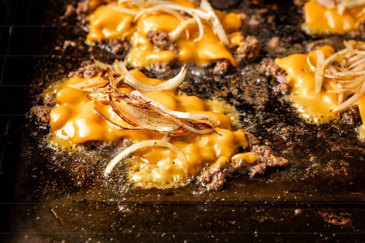 Chopped ground beef on a flat-top grill covered with cheese and onions.