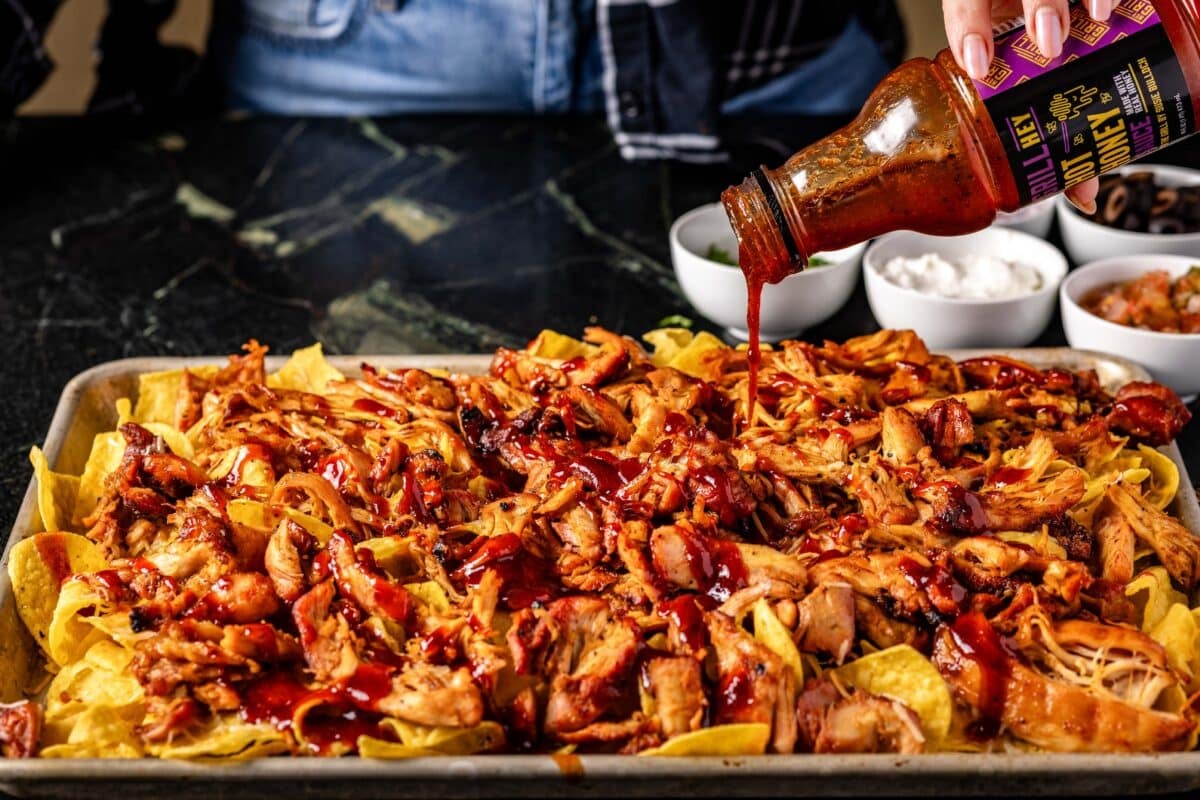 A baking sheet of nachos being drizzled with BBQ sauce.